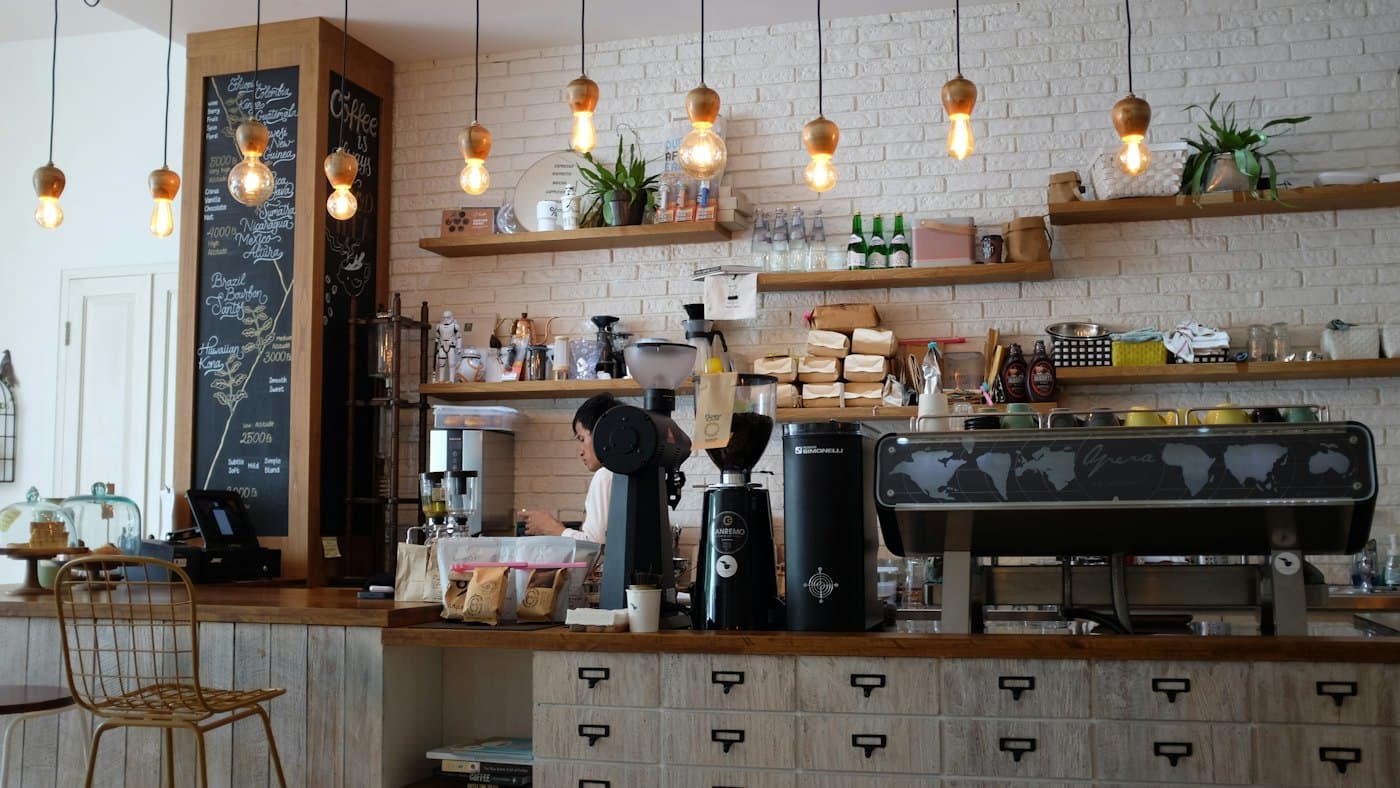 A barista working behind a warm, bright coffee bar under hanging bulbs