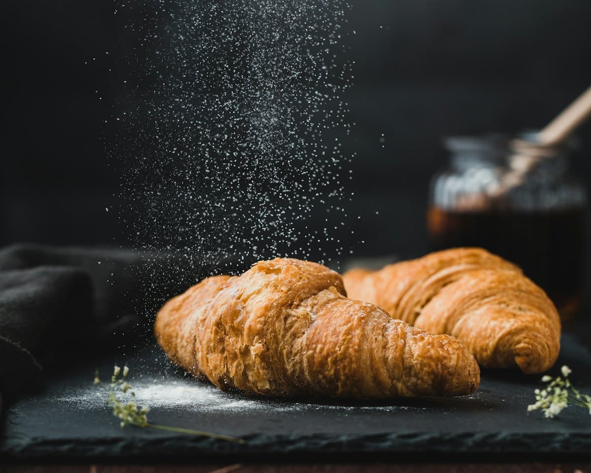 Two golden croissants dusted with flour on a dark slate