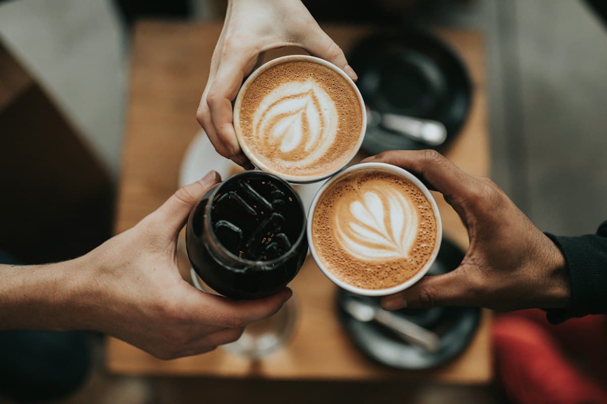 Friends toasting with lattes and a cold coffee over a wooden table