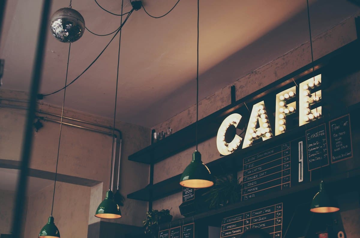 Warm café interior with a lit CAFE sign and pendant lamps