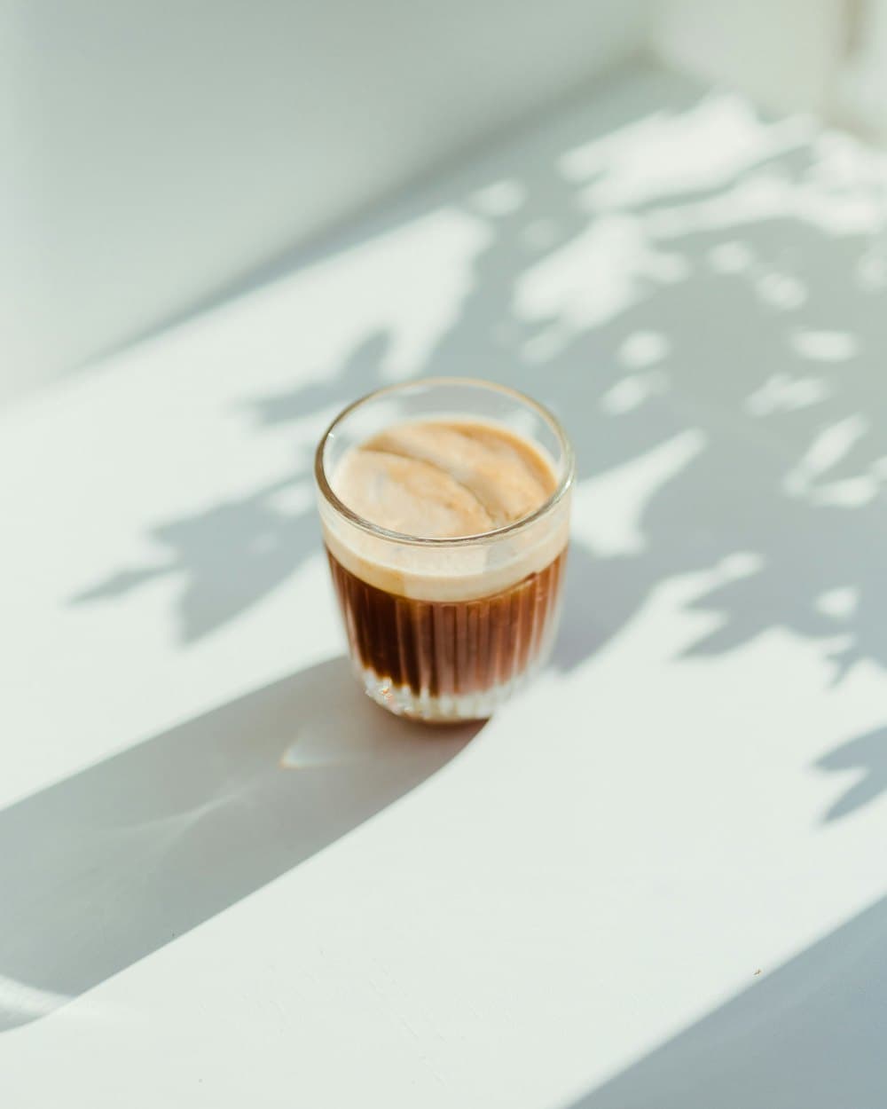 A small glass of coffee in a patch of sunlight with leaf shadows