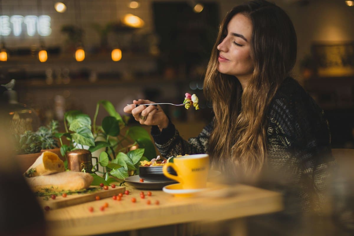 A guest smiling as she enjoys a plate of food at a café table